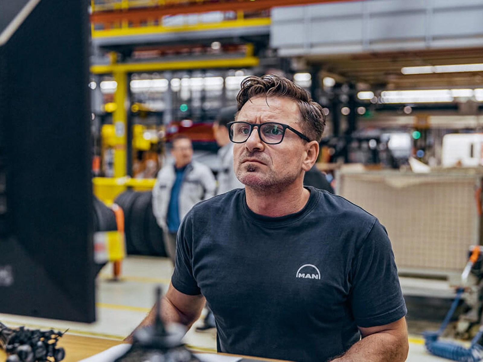 A man in a MAN T-shirt looks intently at a computer screen